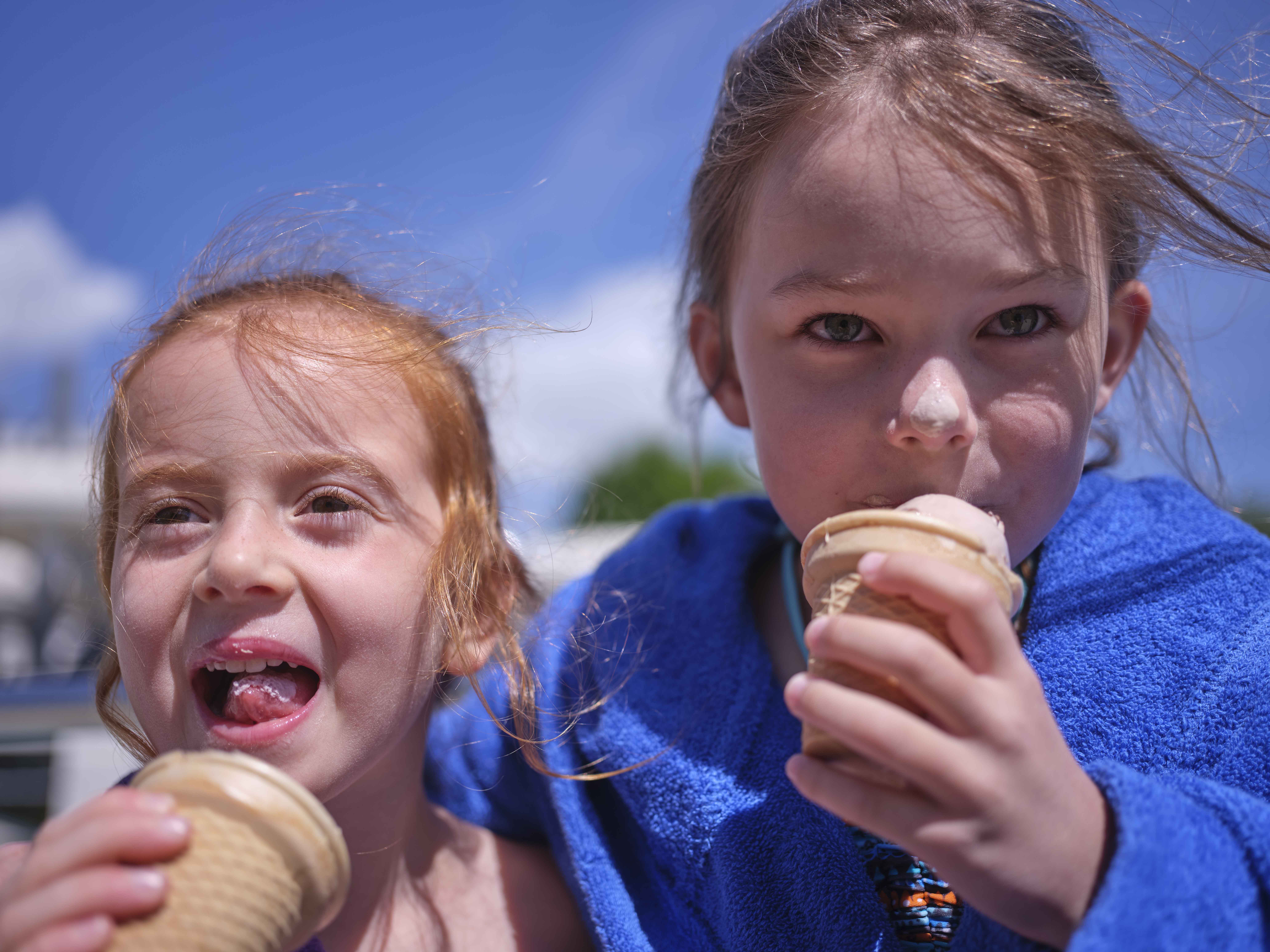 Zwei Mädchen mit Eiscreme vor blauem Himmel.