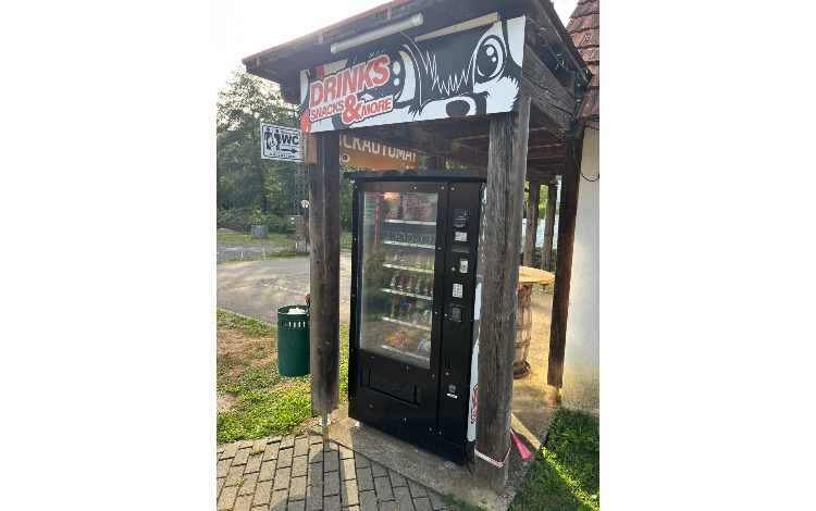 Getränkeautomat mit Schild "DRINKS SNACKS & MORE" und WC-Schild in Österreich