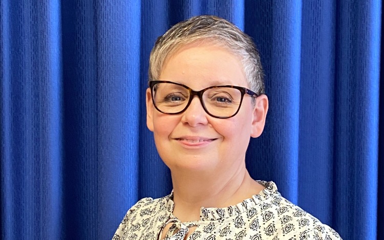 Frau mit Brille und gemustertem Oberteil vor blauem Vorhang