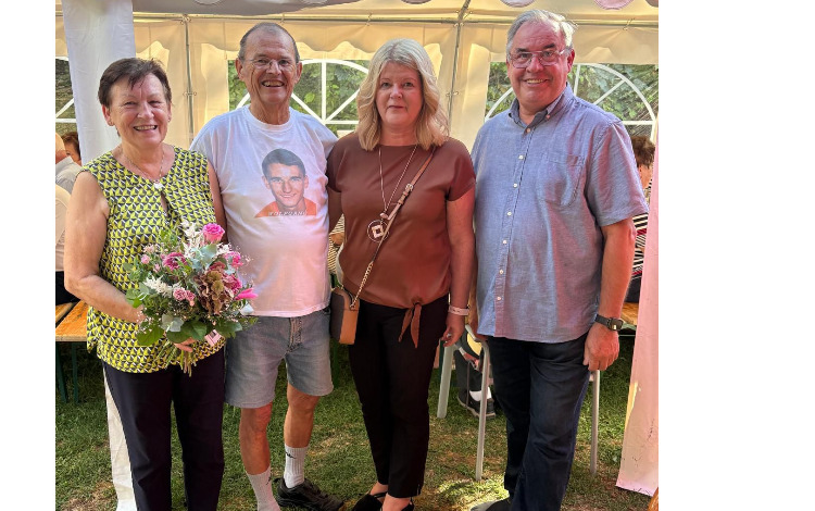 Vier Personen vor einem Zelt, eine Frau hält einen Blumenstrauß