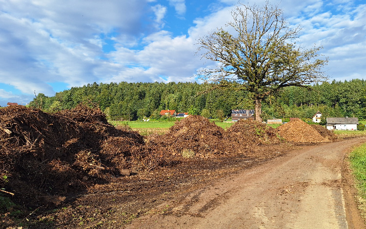 Komposthaufen am Feldweg mit Bäumen und Häusern im Hintergrund