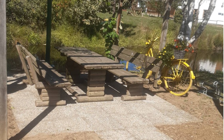 Holz-Sitzgarnitur mit Tisch und gelbem Fahrrad mit Blumen am Ufer