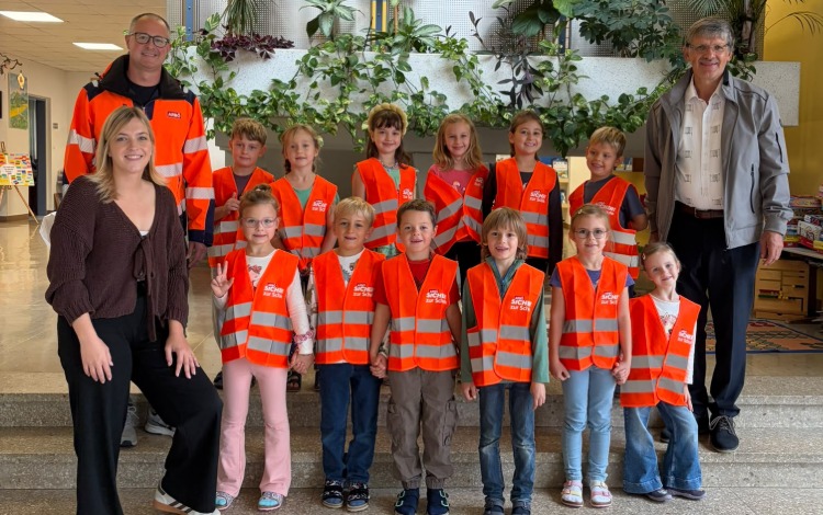 Schülerinnen und Schüler mit Warnwesten vor Schulgebäude, Lehrer und Begleitpersonen.